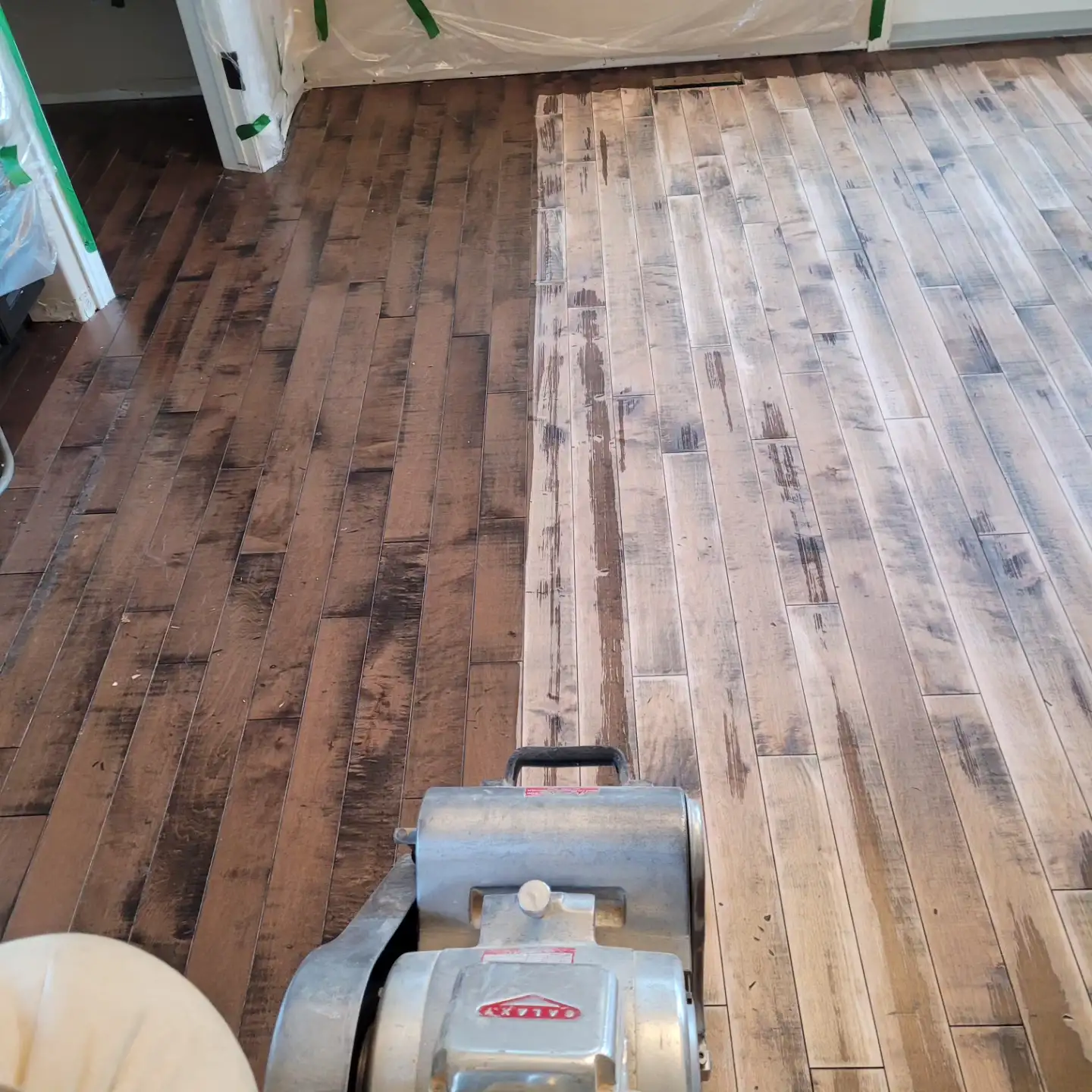 Drum sander part-way across a stained maple floor during refinishing