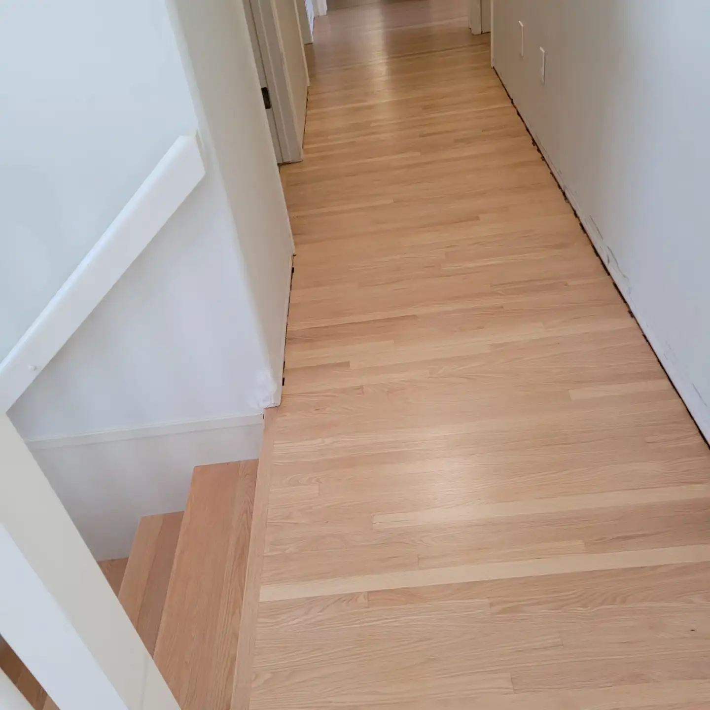 Newly installed oak flooring running down a hallway and onto the stairs